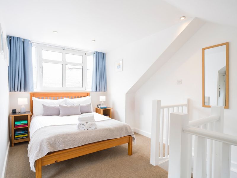 Double bedroom for two with a wooden bed frame, crisp white linen and blue curtains