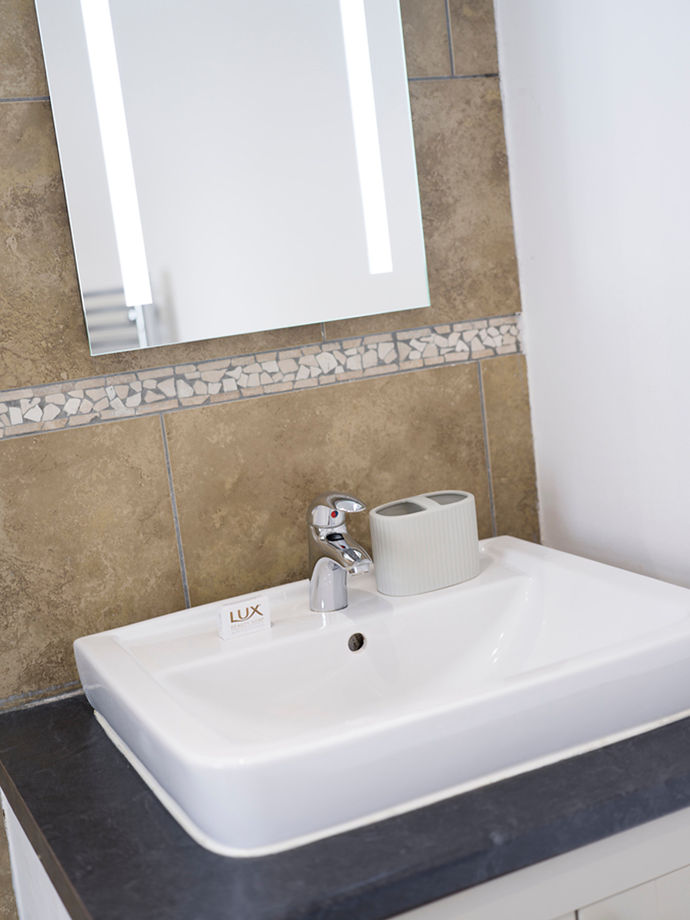 Washbasin on a dark countertop beneath a backlit bathroom mirror
