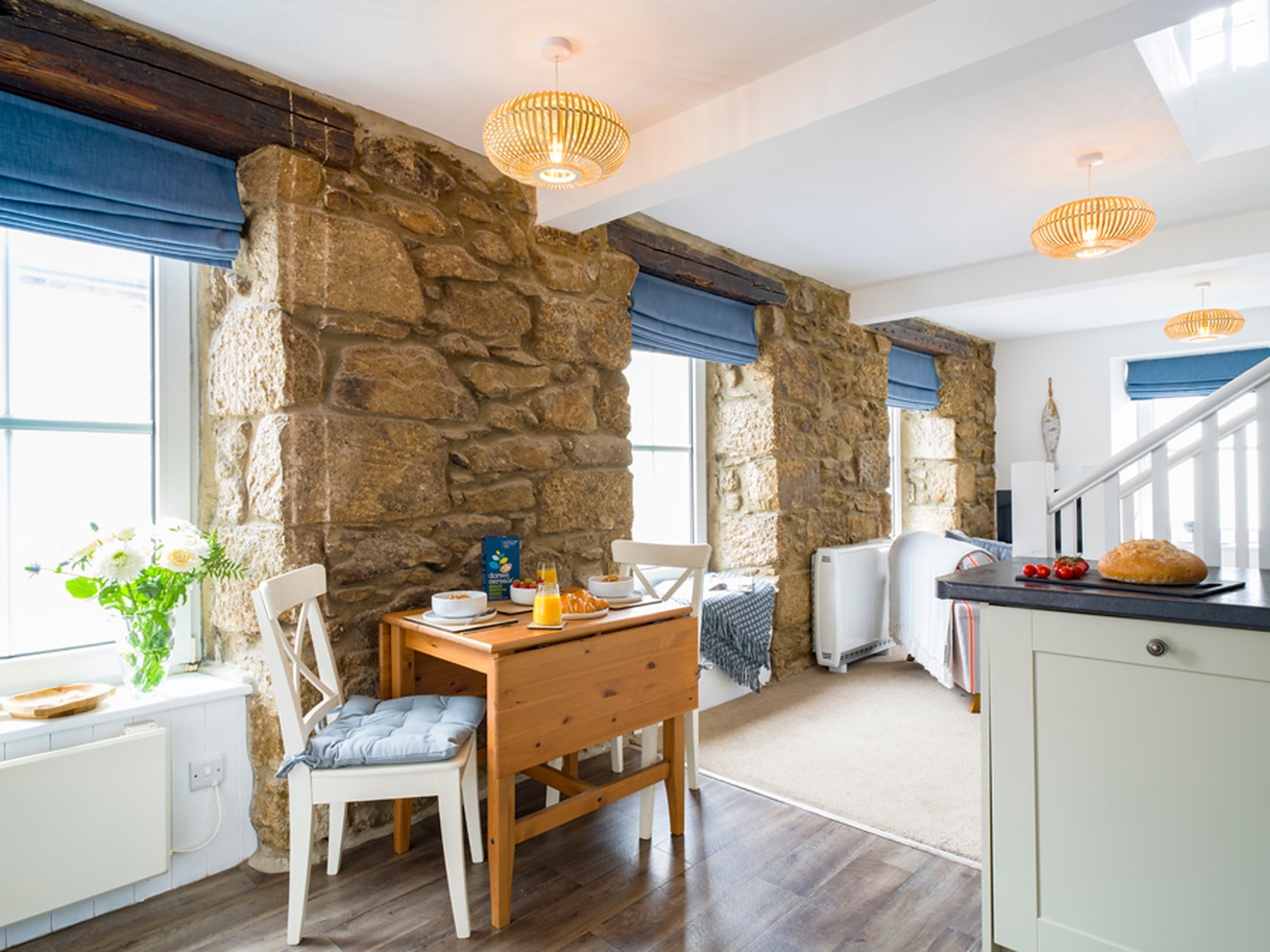 Dining table laid for breakfast beside the exposed stone wall in Little Pearl's open-plan living space