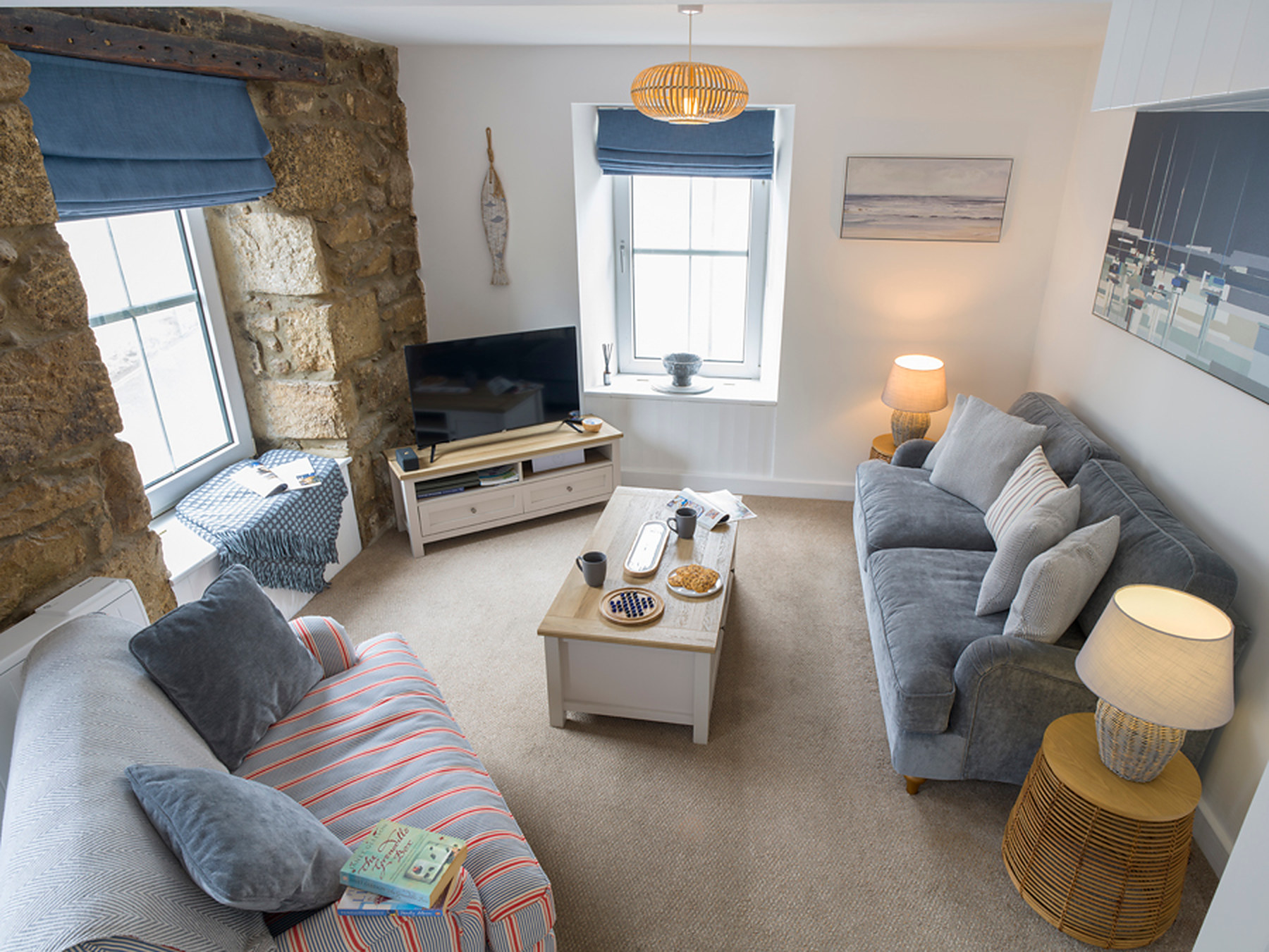 Open-plan sitting area with two sofas, a coffee table and coastal artwork