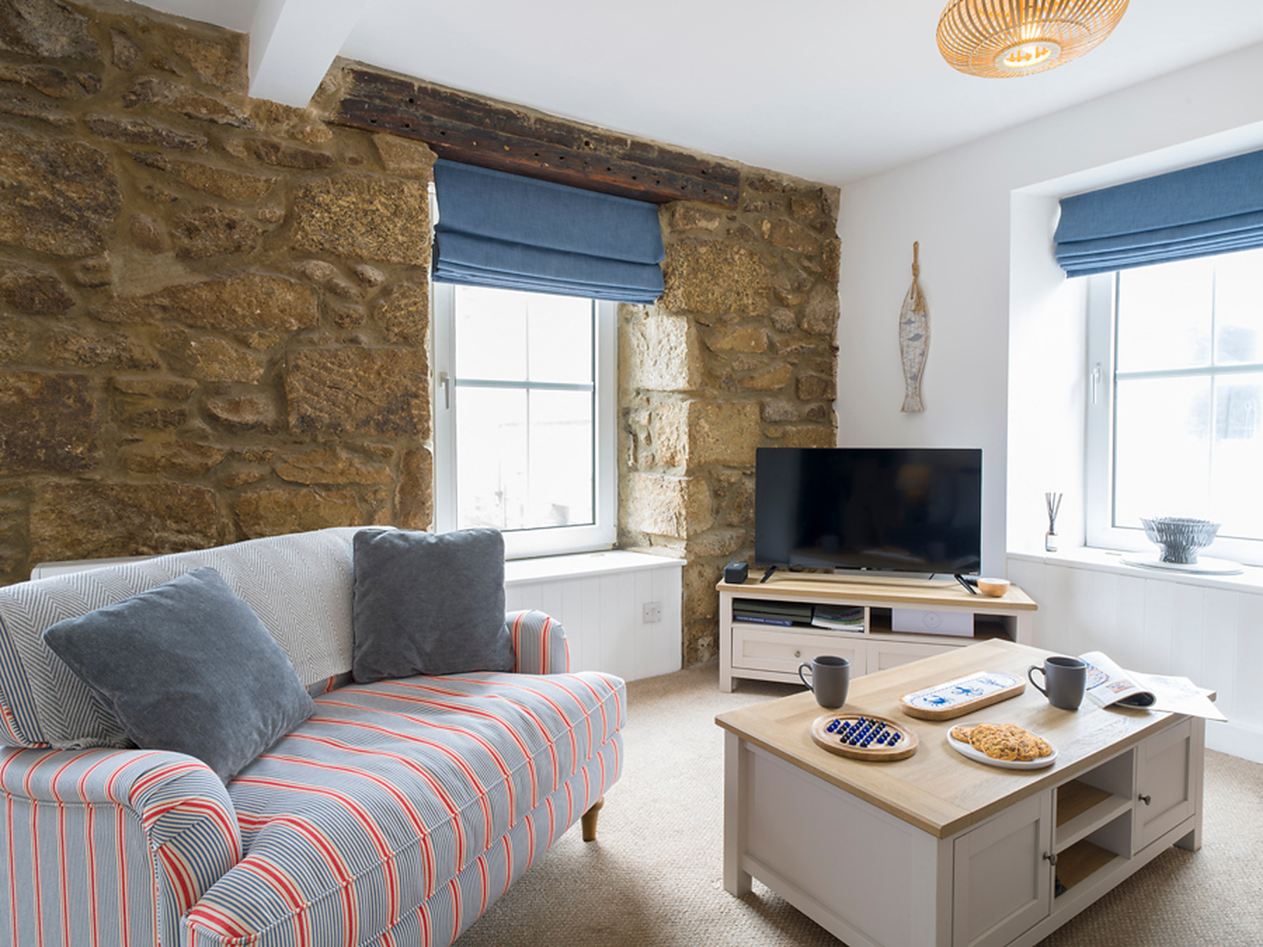 Striped sofa and Smart TV beneath the stone wall and blue roman blinds