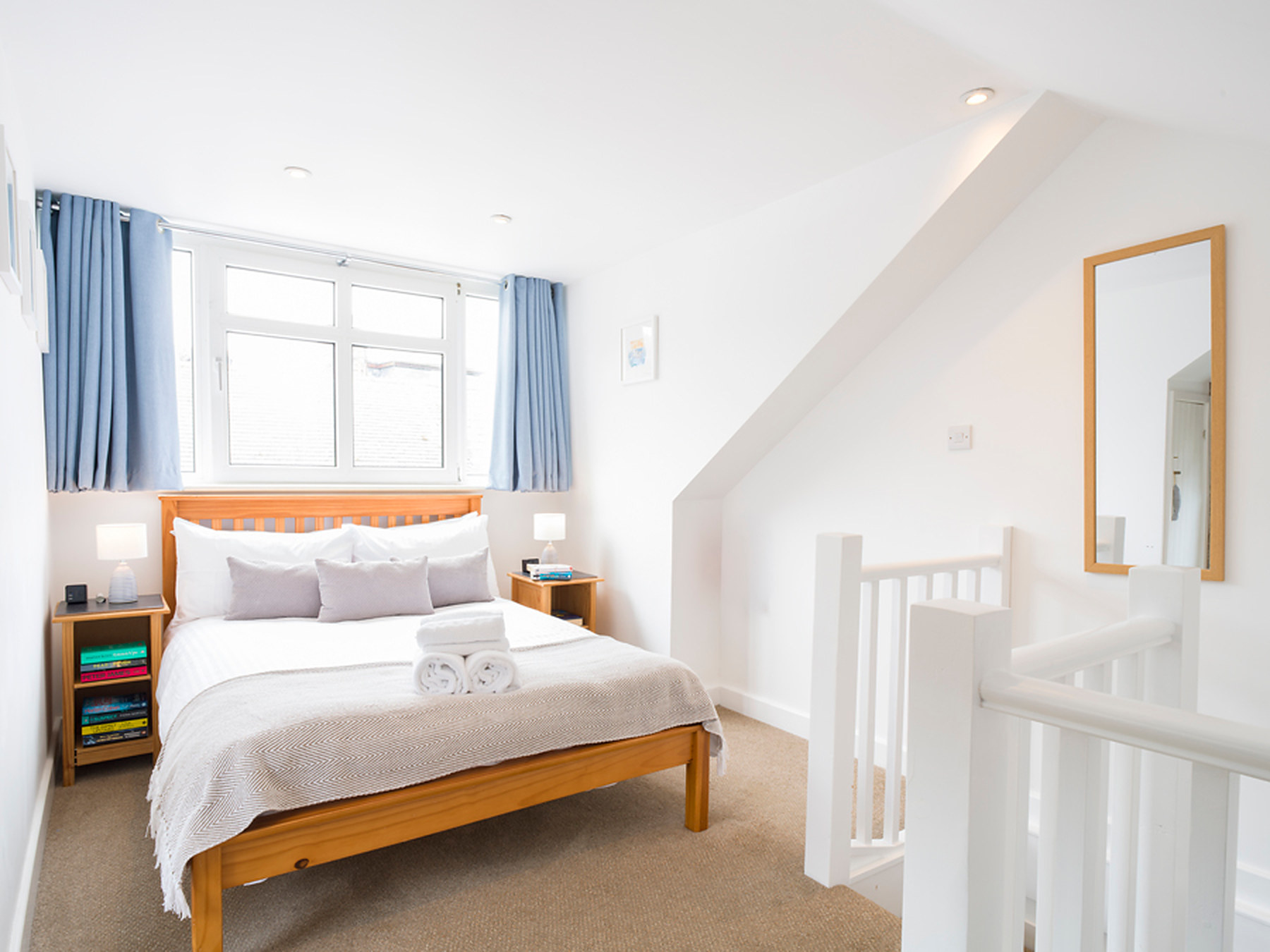 Double bedroom with a wooden bed frame, crisp white linen and blue curtains