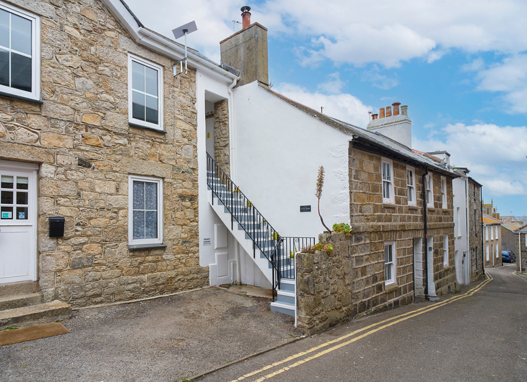 The stone frontage of Little Pearl, with its white-rendered staircase, on a quiet St Ives street
